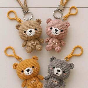 Può includere: Quattro portachiavi a forma di orsetto all'uncinetto in beige, rosa, arancione e grigio. Ogni orsetto ha un viso bianco, occhi neri e la parola "LOVE" cucita sulla pancia. Hanno portachiavi gialli e cinturini simili alla pelle.