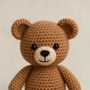 May include: A handmade crochet teddy bear in shades of brown. The bear has a light tan muzzle, black eyes, and a stitched black nose and mouth. The bear's ears are rounded, and the body is textured with visible crochet stitches.