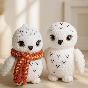 May include: Two handmade white crochet owl figurines. One owl wears a rust-colored scarf with yellow accents. Both owls have black beaks, large brown eyes, and black markings. The owls are on a light brown surface.