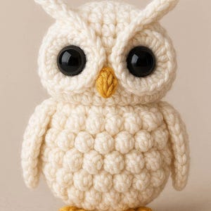 Può includere: Figurina di gufo all'uncinetto fatta a mano, color crema, con grandi occhi neri e un becco e zampe gialle. Il gufo ha un corpo strutturato e arrotondato e piccoli ciuffi di orecchie. Un oggetto decorativo affascinante.