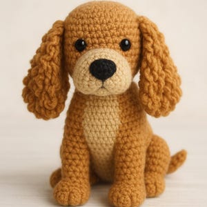 Puede incluir: Un perro de ganchillo hecho a mano en tonos marrón y beige. El perro tiene orejas caídas, una nariz negra y ojos negros. Está sentado con la cola enroscada. Las puntadas de ganchillo texturizadas son visibles. Un juguete encantador.