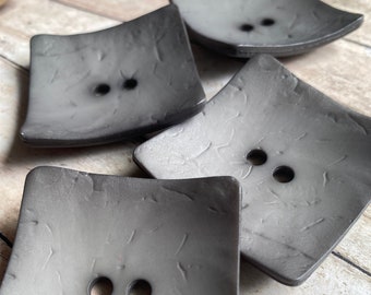 May include: Four grey square buttons with a textured surface and two holes each.