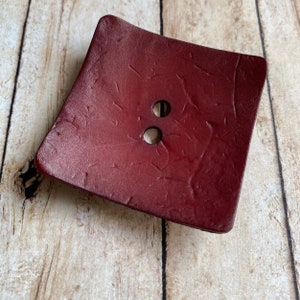 May include: A two-hole burgundy leather button with a textured surface.