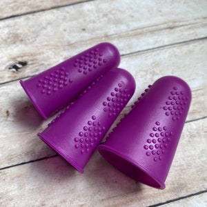 May include: Three purple finger cots with textured surfaces. The finger cots are made of a soft, flexible material.