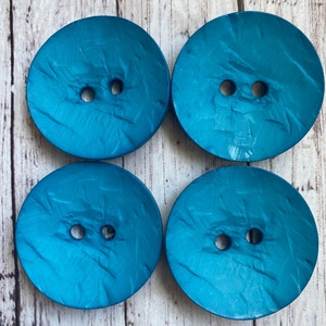 May include: Four teal blue buttons with a textured surface and two holes each.