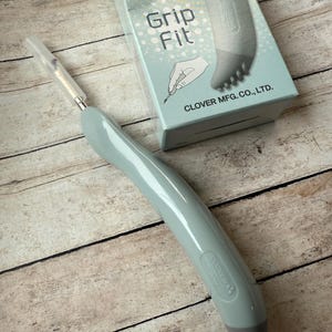 May include: A light blue thread remover with a gray rubber grip and a needle-like tip. The packaging says "Grip Fit" and "Clover Mfg. Co., Ltd."