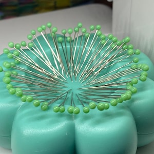 Peut inclure: Un coussin &agrave; &eacute;pingles en plastique vert en forme de fleur avec un grand nombre d'&eacute;pingles &agrave; coudre avec des t&ecirc;tes en verre vert.