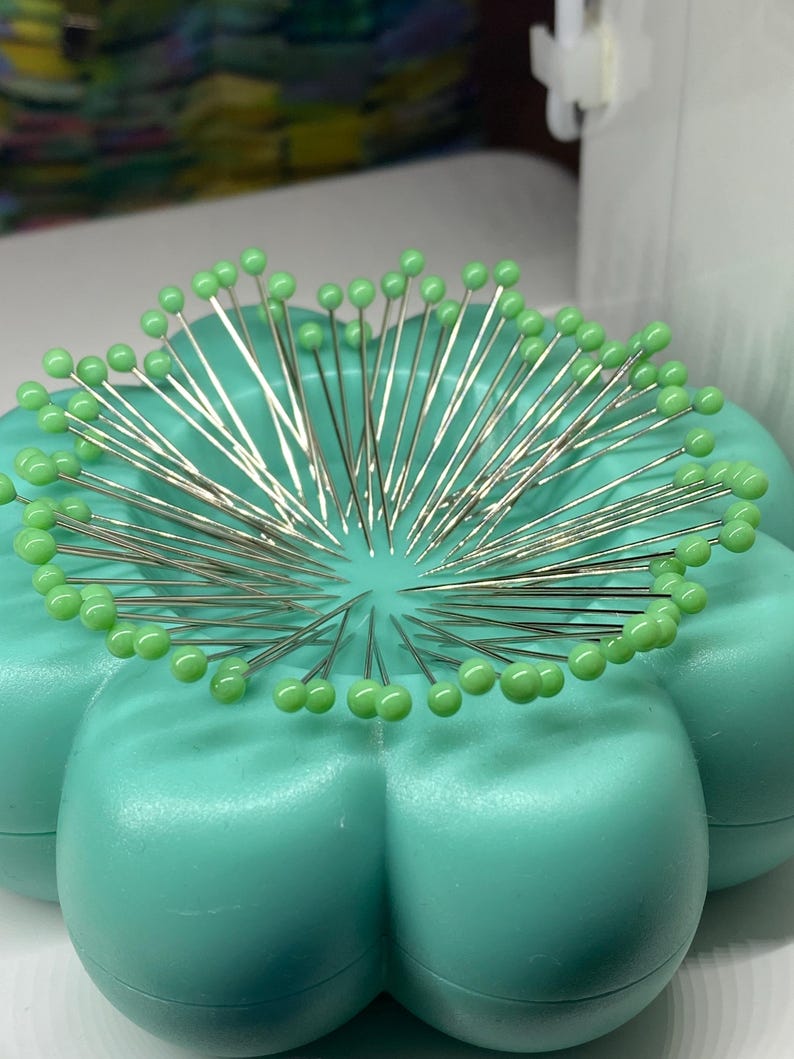 Peut inclure: Un coussin &agrave; &eacute;pingles en plastique vert en forme de fleur avec un grand nombre d'&eacute;pingles &agrave; coudre avec des t&ecirc;tes en verre vert.