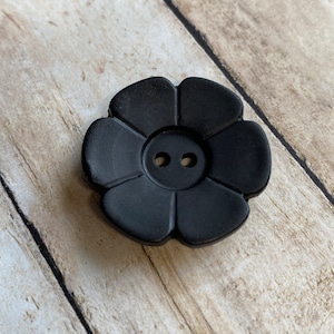 May include: A black plastic flower-shaped button with two holes.