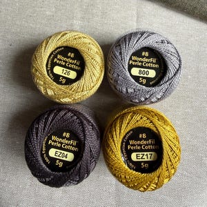 May include: Four round balls of WonderFil Perle Cotton thread, size #8, 5g each. The colors are gold, silver, dark charcoal, and mustard yellow. Each label reads 100% Egyptian Cotton and displays the specific color code: 126, 800, EZ04, and EZ17.