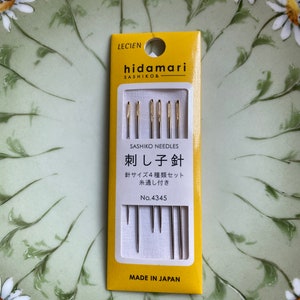 May include: A yellow and white package of sashiko needles, with the brand name "hidamari" and the text "SASHIKO NEEDLES" visible. The package contains four different sizes of needles. The text "MADE IN JAPAN" is printed at the bottom.