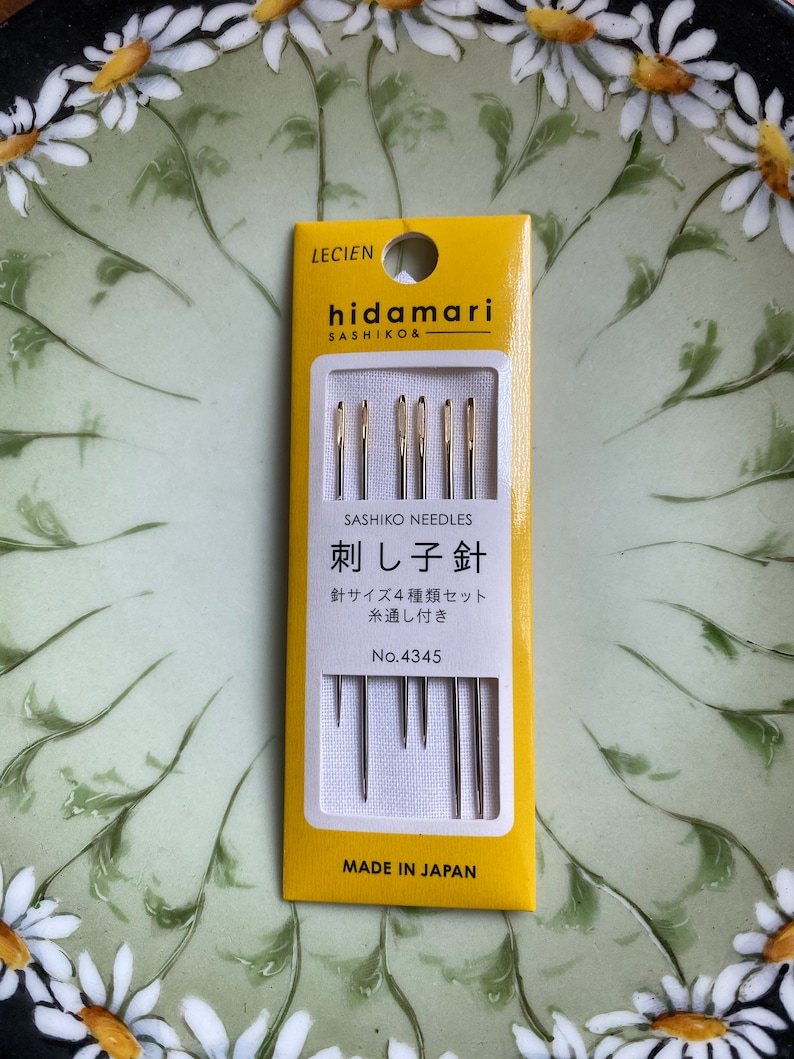 May include: A yellow and white package of sashiko needles, with the brand name "hidamari" and the text "SASHIKO NEEDLES" visible. The package contains four different sizes of needles. The text "MADE IN JAPAN" is printed at the bottom.