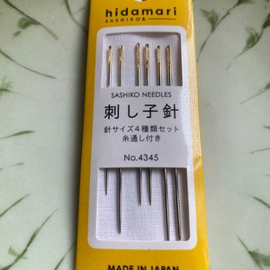 May include: A yellow and white package of sashiko needles. The package has the brand name "hidamari" and the text "SASHIKO NEEDLES" printed on it. The package contains several needles with gold-colored eyes. The text "MADE IN JAPAN" is printed at the bottom.