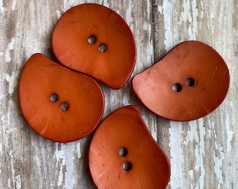 May include: Four orange-brown, two-hole, irregularly shaped buttons. The buttons have a textured surface and a slightly raised edge.