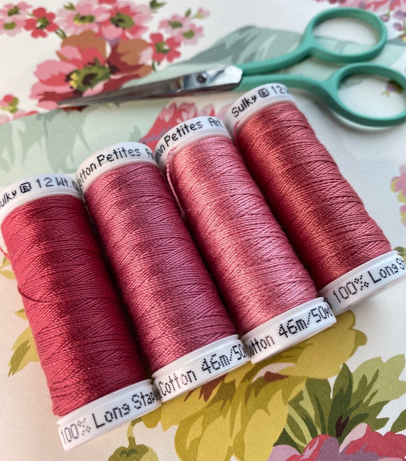 May include: Four spools of Sulky 12wt cotton thread in a dusty rose color. The spools are labeled "100% Long Staple Cotton 46m/50m".