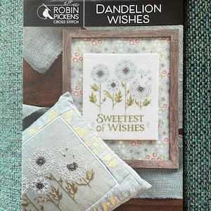 May include: A cross-stitch pattern titled "Dandelion Wishes" by Robin Pickens. The image features a framed cross-stitch design with dandelions and the text "Sweetest of Wishes." A matching pillow with a dandelion design is also visible.