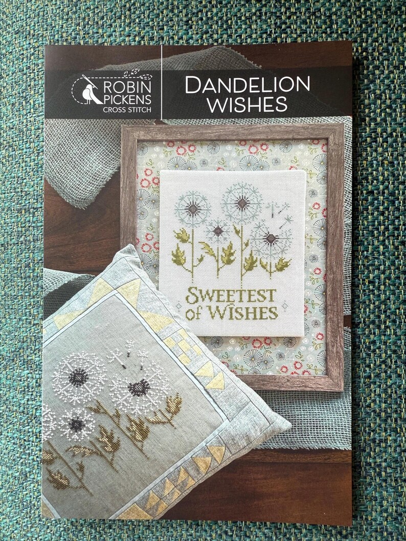 May include: A cross-stitch pattern titled "Dandelion Wishes" by Robin Pickens. The image features a framed cross-stitch design with dandelions and the text "Sweetest of Wishes." A matching pillow with a dandelion design is also visible.
