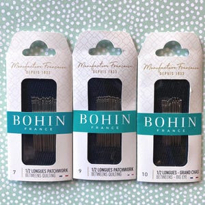 May include: Three packages of Bohin sewing needles, labeled with the size and type of needle. The packages are white with blue and gold accents. The text on the packages reads "Manufacture Française Depuis 1833" and "BOHIN FRANCE".
