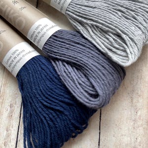 May include: Three spools of cotton embroidery floss, one gray, one light blue, and one dark blue. Each spool has a label that reads "Cotton 100% Made in Japan" and includes a website address.
