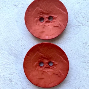May include: Two large, round, orange buttons with a textured surface and two holes in the center.