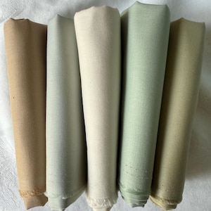 May include: Five folded pieces of fabric arranged vertically in a row. The colors from left to right are a warm tan, a light cool gray, a creamy off-white, a soft sage green, and a muted olive green. Each piece of fabric has a smooth texture.