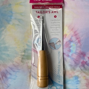 May include: A wooden-handled tailor's awl with a metal point, packaged in a clear plastic bag. The packaging includes instructions for using the tool to press overlapping fabrics gently to make sewing more smoothly. The packaging also includes the text "Sew Mate" and "Tooltron Creative Tools".