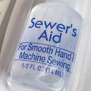 May include: A clear plastic bottle of Sewer's Aid sewing machine lubricant. The bottle is labeled "Sewer's Aid" in blue lettering and says "For Smooth Hand & Machine Sewing 1/2 FL OZ (14 ML)".