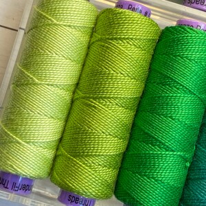 Puede incluir: Cuatro carretes de hilo de bordar verde, cada uno con un tono de verde diferente. Los carretes est&aacute;n etiquetados como "WonderFil", "Threads", "WonderFil" y "Threads".