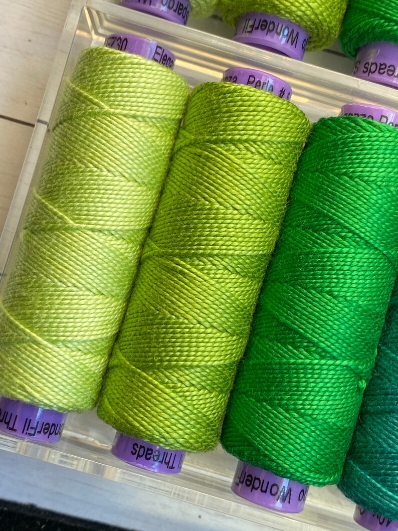 Puede incluir: Cuatro carretes de hilo de bordar verde, cada uno con un tono de verde diferente. Los carretes est&aacute;n etiquetados como "WonderFil", "Threads", "WonderFil" y "Threads".
