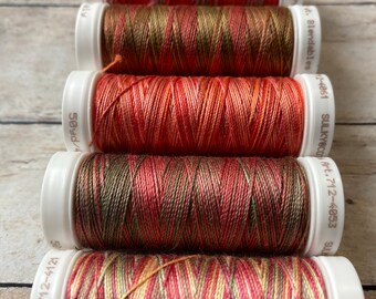 May include: Five spools of Sulky thread in shades of red, orange, green, and gold. The thread is variegated and has a subtle shimmer. The spools are labeled with the Sulky brand name and the thread art number.