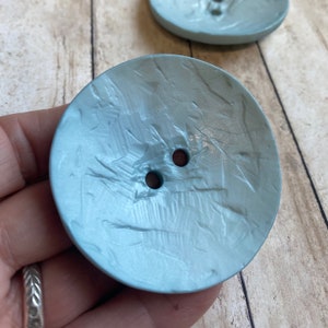 May include: Two light blue, round, textured buttons with two holes each.
