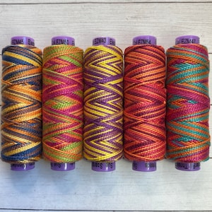 May include: Five spools of colorful embroidery thread with a chevron pattern. The spools are labeled with the brand name "Sue Thread" and the color numbers EZM45, EZM50, EZM43, EZM54, and EZM47.