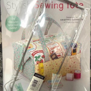 May include: A packaged sewing tote with a floral and strawberry design. The tote includes wire frames and a hoop pull zipper. The packaging reads "Stylish Sewing Tote" and "Try this new large size caddy!" The tote measures 10 x 3 5/8 inches.