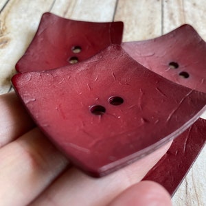 May include: Three red, square-shaped buttons with a textured surface. Each button has two holes.