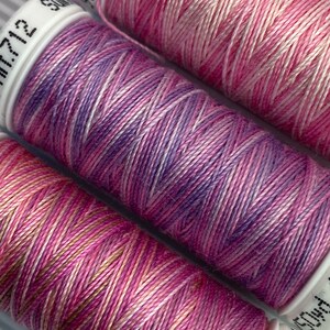 May include: Three spools of embroidery floss in shades of pink, purple, and white. The floss is wound around white spools with black text.