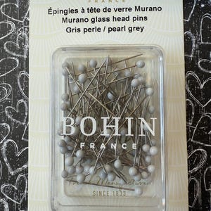 Peut inclure: Un paquet de 60 &eacute;pingles &agrave; t&ecirc;te de verre Murano gris perle de Bohin France. Les &eacute;pingles sont dans un r&eacute;cipient en plastique transparent. L'emballage indique "&Eacute;pingles &agrave; t&ecirc;te de verre Murano Murano glass head pins Gris perle / pearl grey" et "Acier nickel&eacute;/Nickel plated steel".