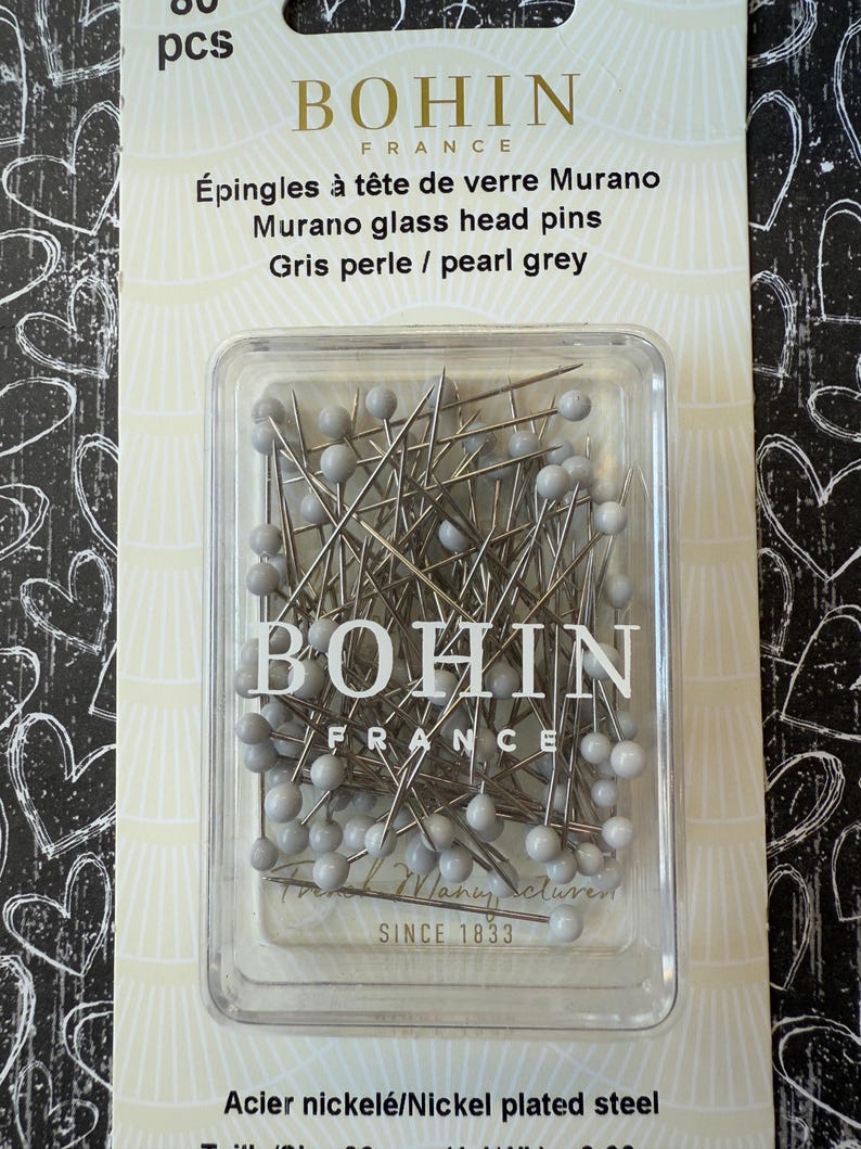 Peut inclure: Un paquet de 60 &eacute;pingles &agrave; t&ecirc;te de verre Murano gris perle de Bohin France. Les &eacute;pingles sont dans un r&eacute;cipient en plastique transparent. L'emballage indique "&Eacute;pingles &agrave; t&ecirc;te de verre Murano Murano glass head pins Gris perle / pearl grey" et "Acier nickel&eacute;/Nickel plated steel".