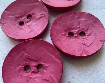 May include: Four large, round, raspberry-colored buttons with two holes each. The buttons have a textured surface and a slightly glossy finish. These buttons are suitable for sewing projects and crafts.