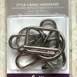 May include: A kit of silver-coloured metal purse hardware in a clear plastic package labelled Style 4 Basic Hardware, 1 Inch. The set includes several lobster claw clasps and rectangular rings for bag construction, visible through the clear blister pack.