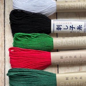May include: Five spools of sashiko thread in white, black, green, red, and dark green. Each spool is labeled with the Japanese text "刺し子糸" which translates to "Sashiko thread" and the brand name "SASHIKO".