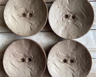 May include: Four large, round, brown buttons with a textured surface. Each button has two holes in the center.