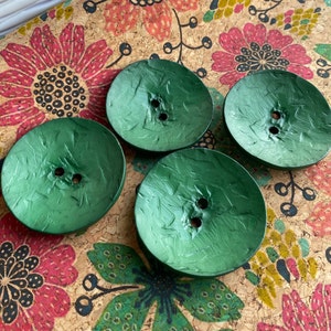 May include: Four green, round, textured buttons with two holes each. The buttons have a metallic sheen.