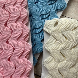 May include: Three rolls of wavy trim in pink, blue, and white. The trim is made of a woven fabric and has a scalloped edge. The trim is labeled with the number "402 061".