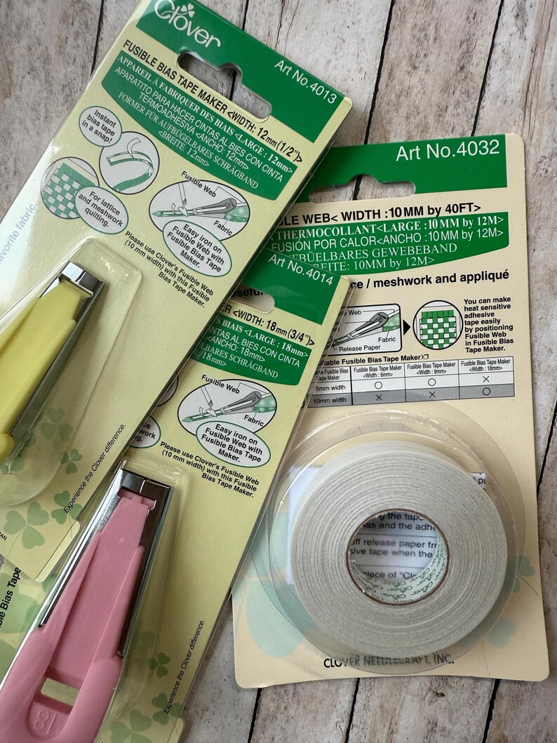 May include: An assortment of Clover brand sewing tools, including fusible bias tape makers and fusible web tape. The packaging is green and white, with product details and instructions. The tools are yellow and pink.