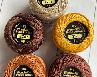 May include: Five spools of WonderFil #8 Perle Cotton thread in various earth-tone colors. The spools are labeled with color codes and weights. Colors include gold, brown, and orange. The thread is 100% Egyptian cotton.