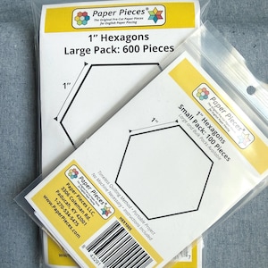 May include: Two clear plastic bags containing pre-cut paper hexagons for quilting. The larger bag is labeled 1" Hexagons Large Pack: 600 Pieces. The smaller bag is labeled 1" Hexagons Small Pack: 100 Pieces. Both feature the Paper Pieces logo and text.