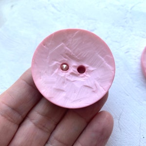 May include: A pink plastic button with a textured surface and two holes.
