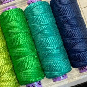 Puede incluir: Cuatro carretes de hilo en tonos verdes y azules. Los carretes est&aacute;n etiquetados como "Elegance", "Wonder", "Elegance" y "Wonder".