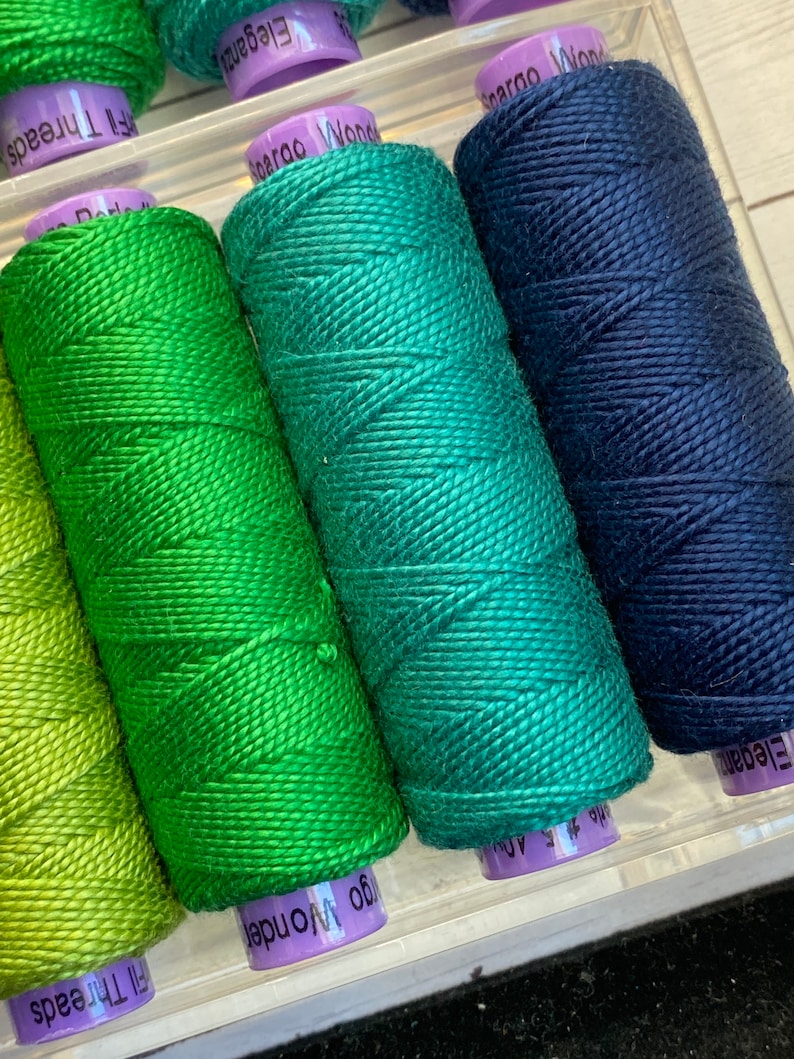 Puede incluir: Cuatro carretes de hilo en tonos verdes y azules. Los carretes est&aacute;n etiquetados como "Elegance", "Wonder", "Elegance" y "Wonder".