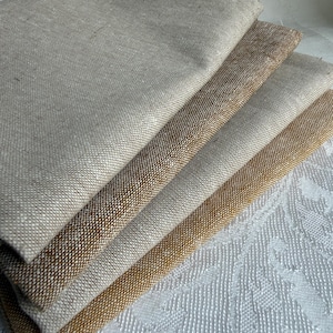 K&ouml;nnte beinhalten: Ein Stapel aus vier gefalteten Stoffmustern mit einer sichtbaren Webstruktur. Die Farben reichen von hellem Beige und Haferfarben bis hin zu Mittelbraun und einem tieferen Goldbraun, was eine nat&uuml;rliche, erdige Farbpalette unterstreicht.